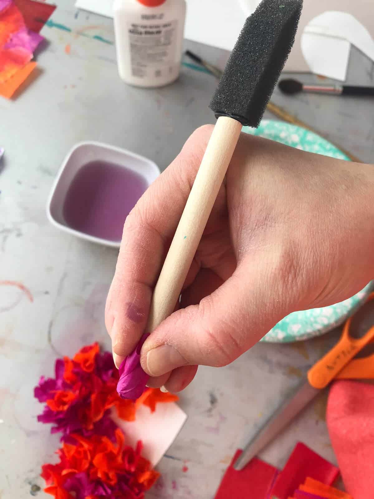 hand holding brush with tissue paper on the end working on heart craft.