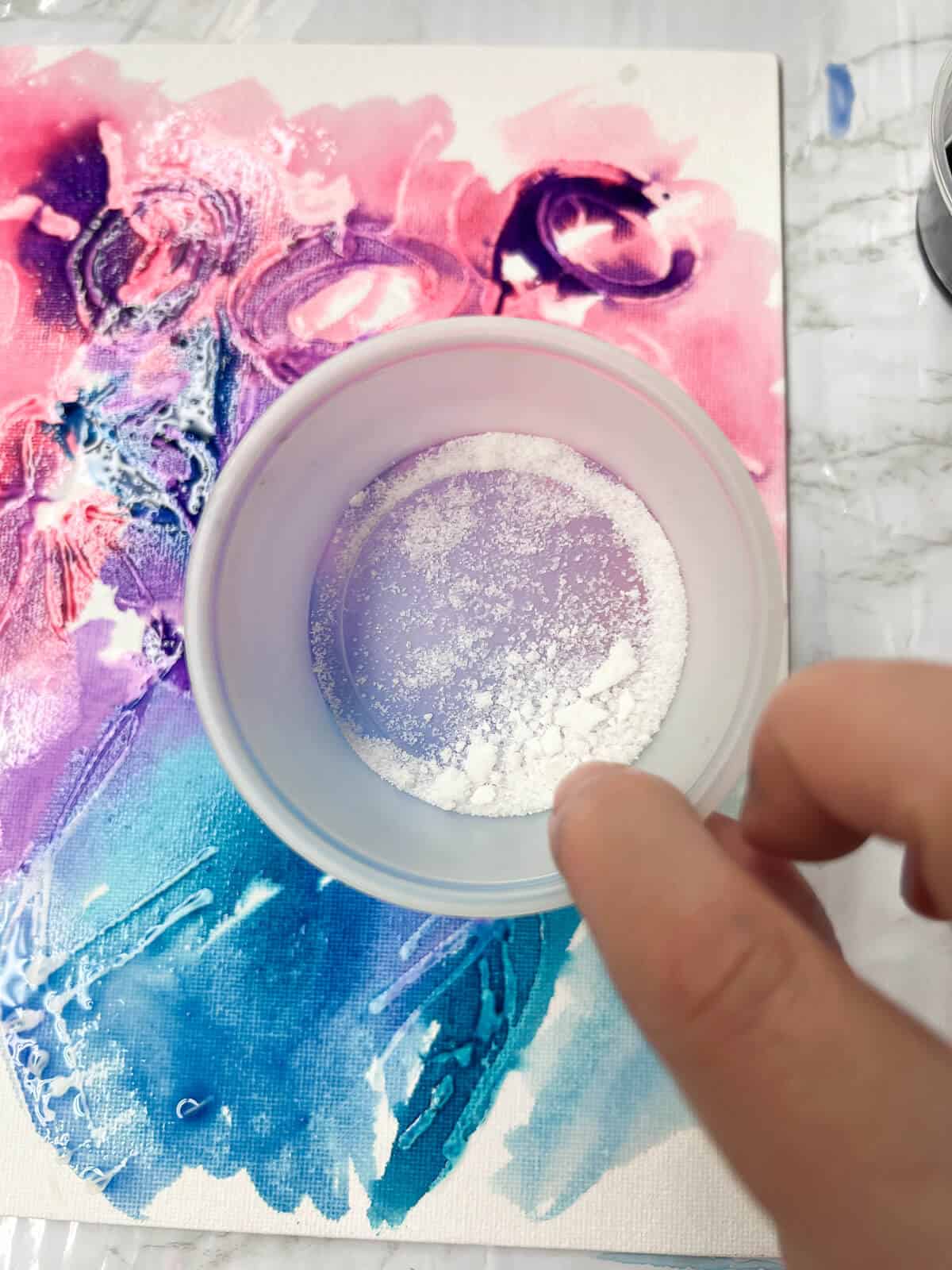 salt in a little cup being on top of watercolor painting done with glue and liquid watercolor paint.