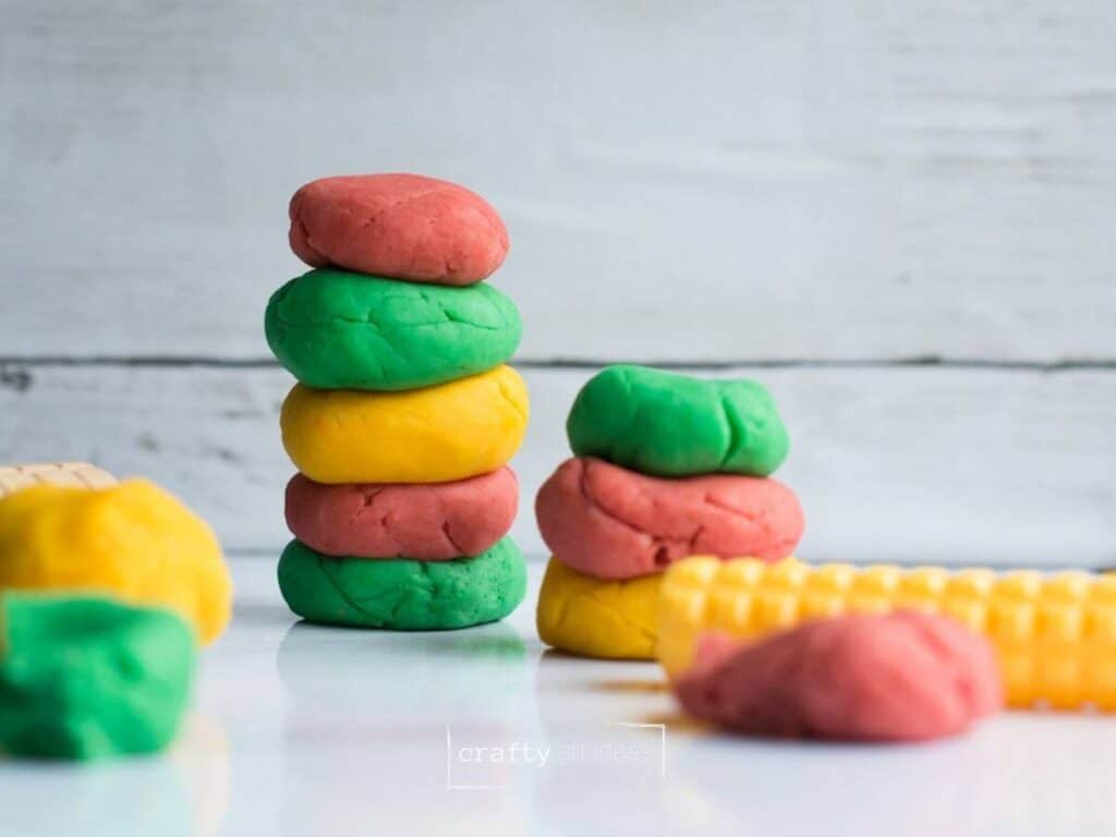 red, green, yellow homemade playdough made in slower cooker on white marble with shiplap background.
