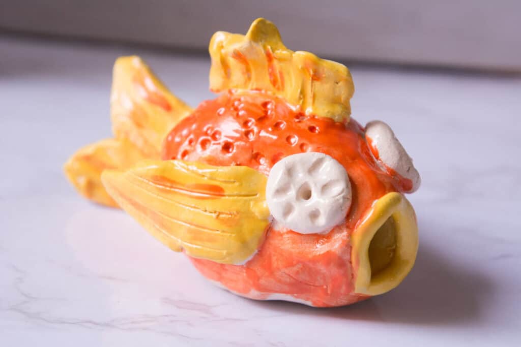 clay fish art lesson made from two pinch pots glazed with orange and yellow glaze.