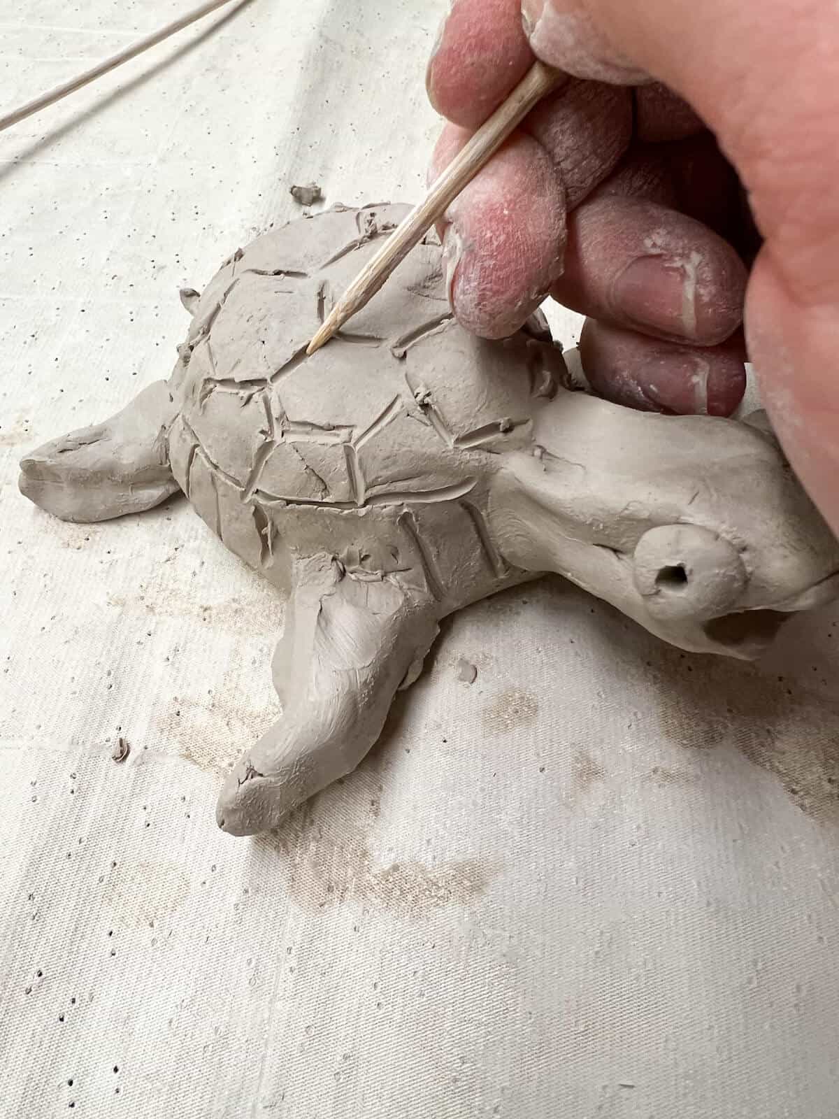 hand holding wooden skewer and drawing hexagons on clay turtle shell.