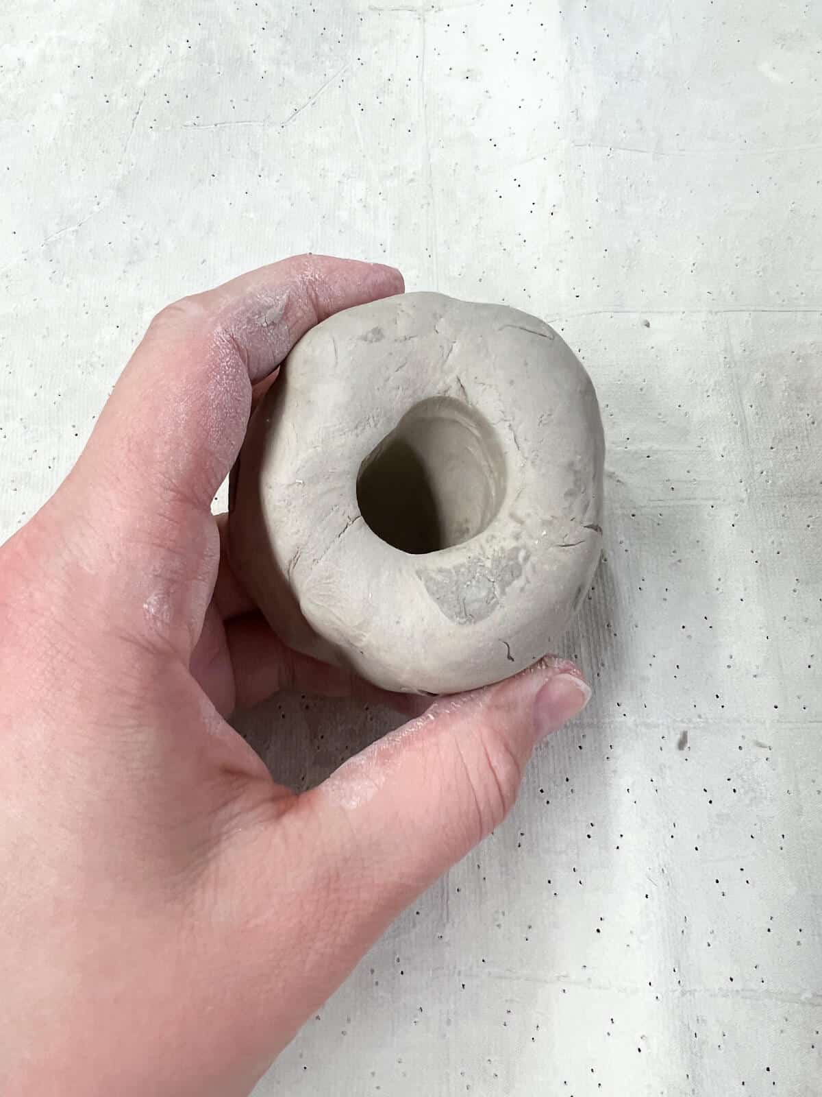 hand holding ball of clay with thumb hole pushed in.