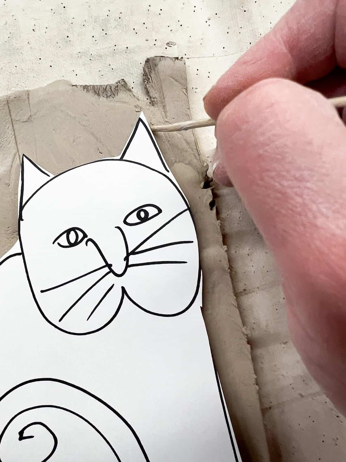 hand using wooden skewer to cut around paper cat template.