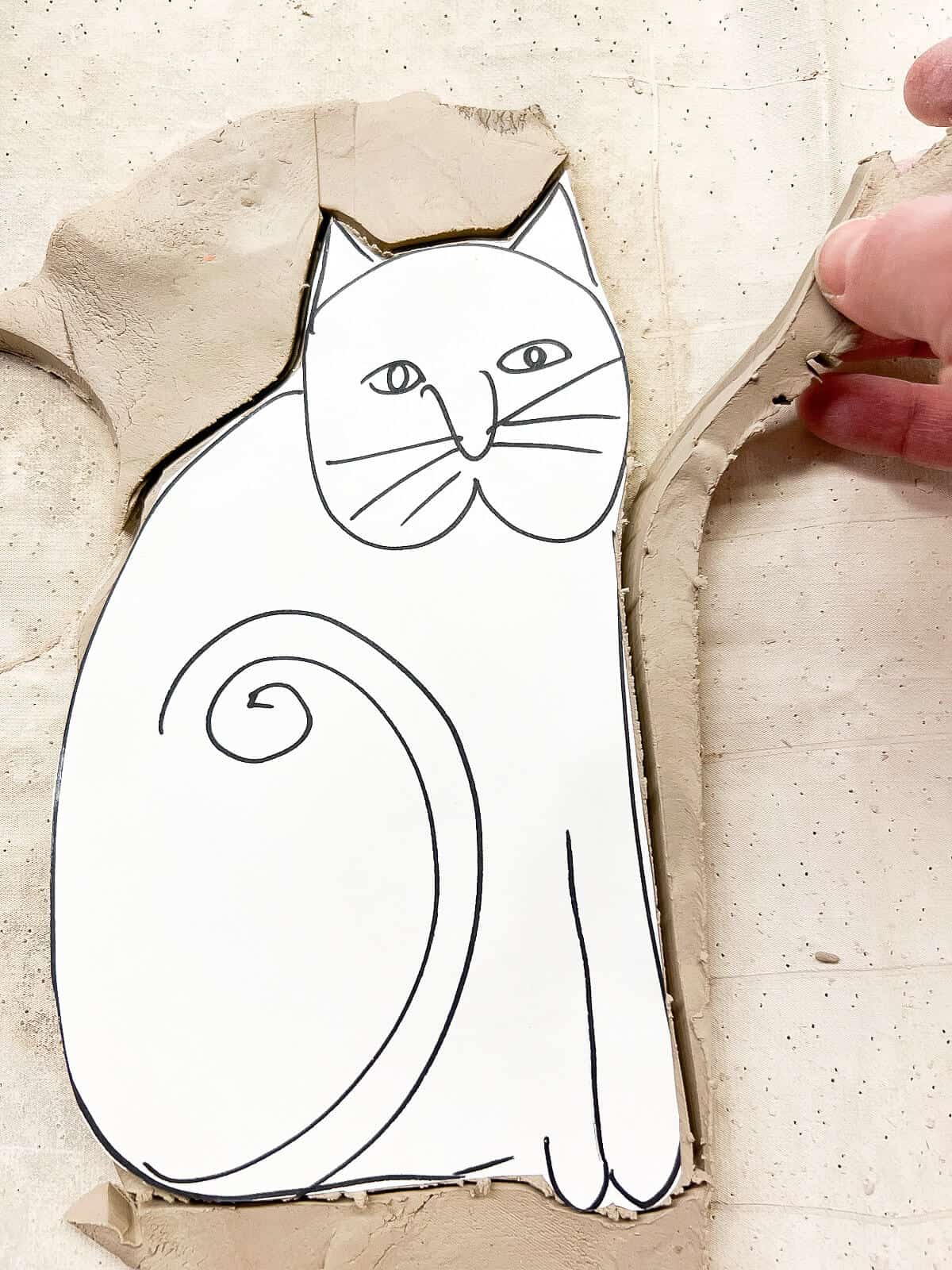hand pulling extra cut clay off of cut out cat.