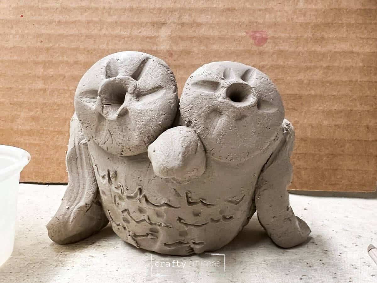 clay owl pinch pot with clay eyes, wings and beak on clay placemat.