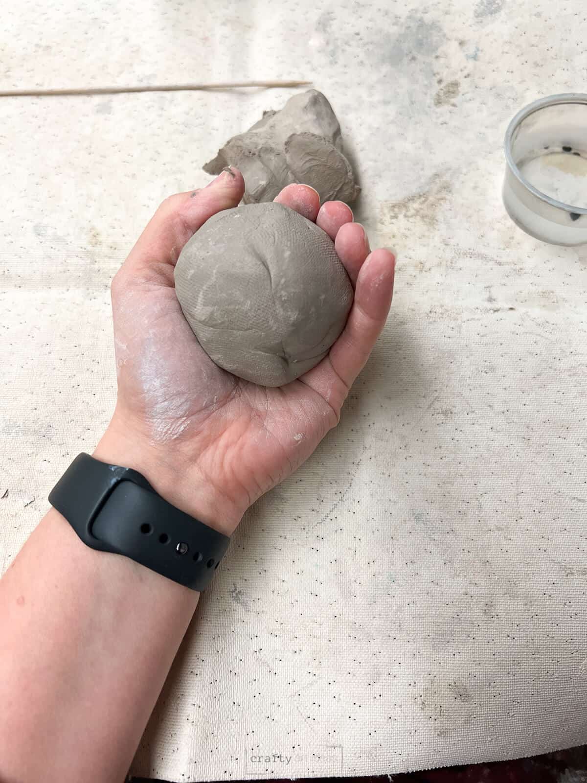 Ball of clay in hand over clay placemat.