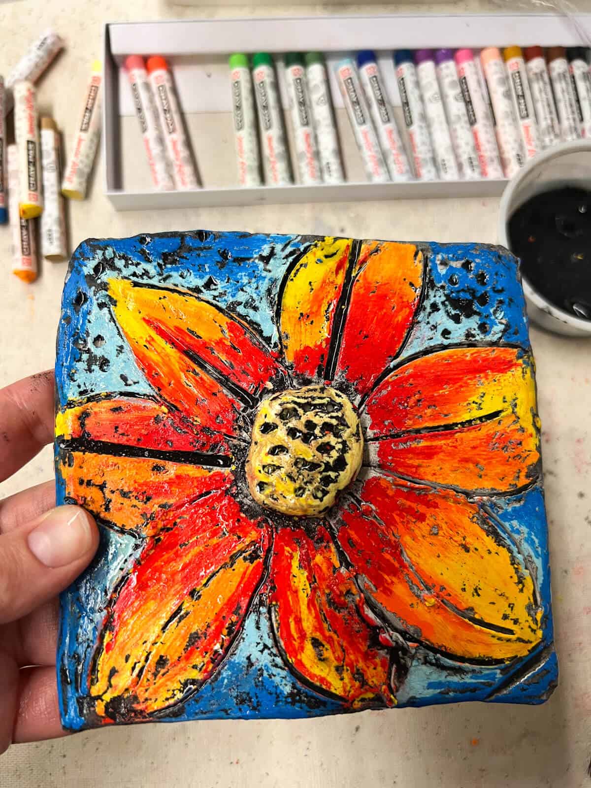 clay flower relief tile after oil pastel and black paint resist applied.