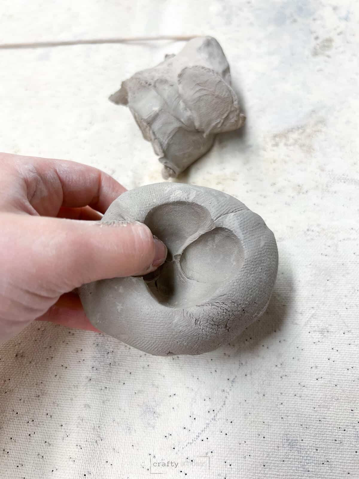 thumb pushing in 4 thumbprints in clay ball to start making pinch pot.