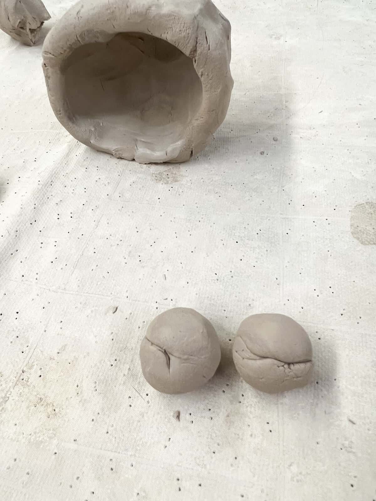 two small balls of clays to become clay monster eyes in front of pinch pot on its side.
