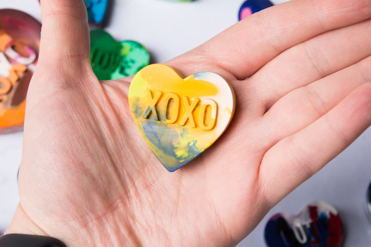 xoxo heart crayon with yellow, green and white in hand.