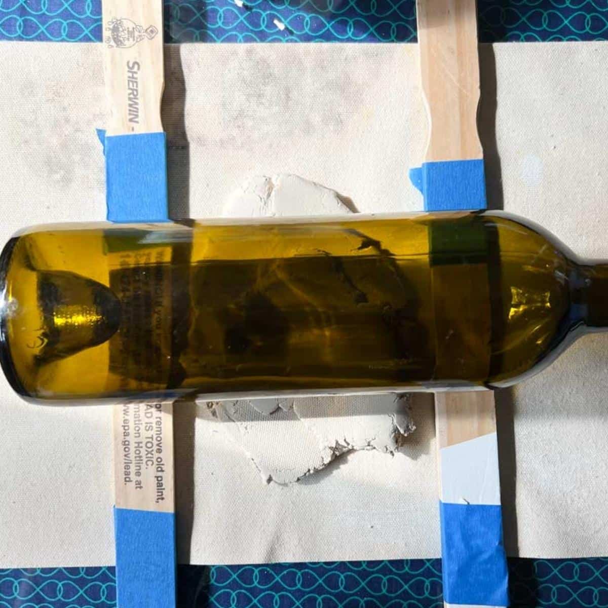 clay, glass bottle and taped wooden sticks together on a table.