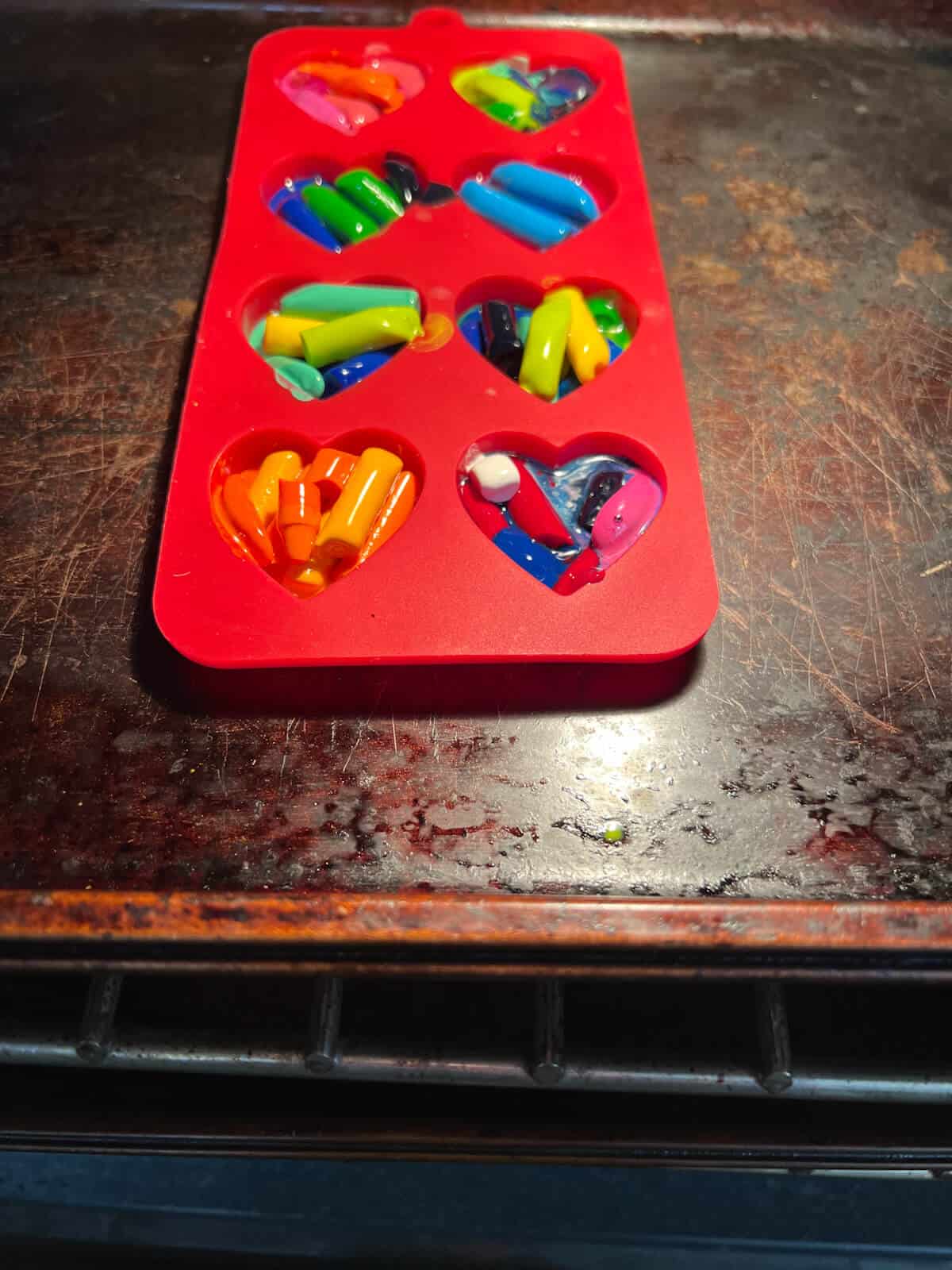 heart silicone mold on cookie sheet in oven with crayons melting.