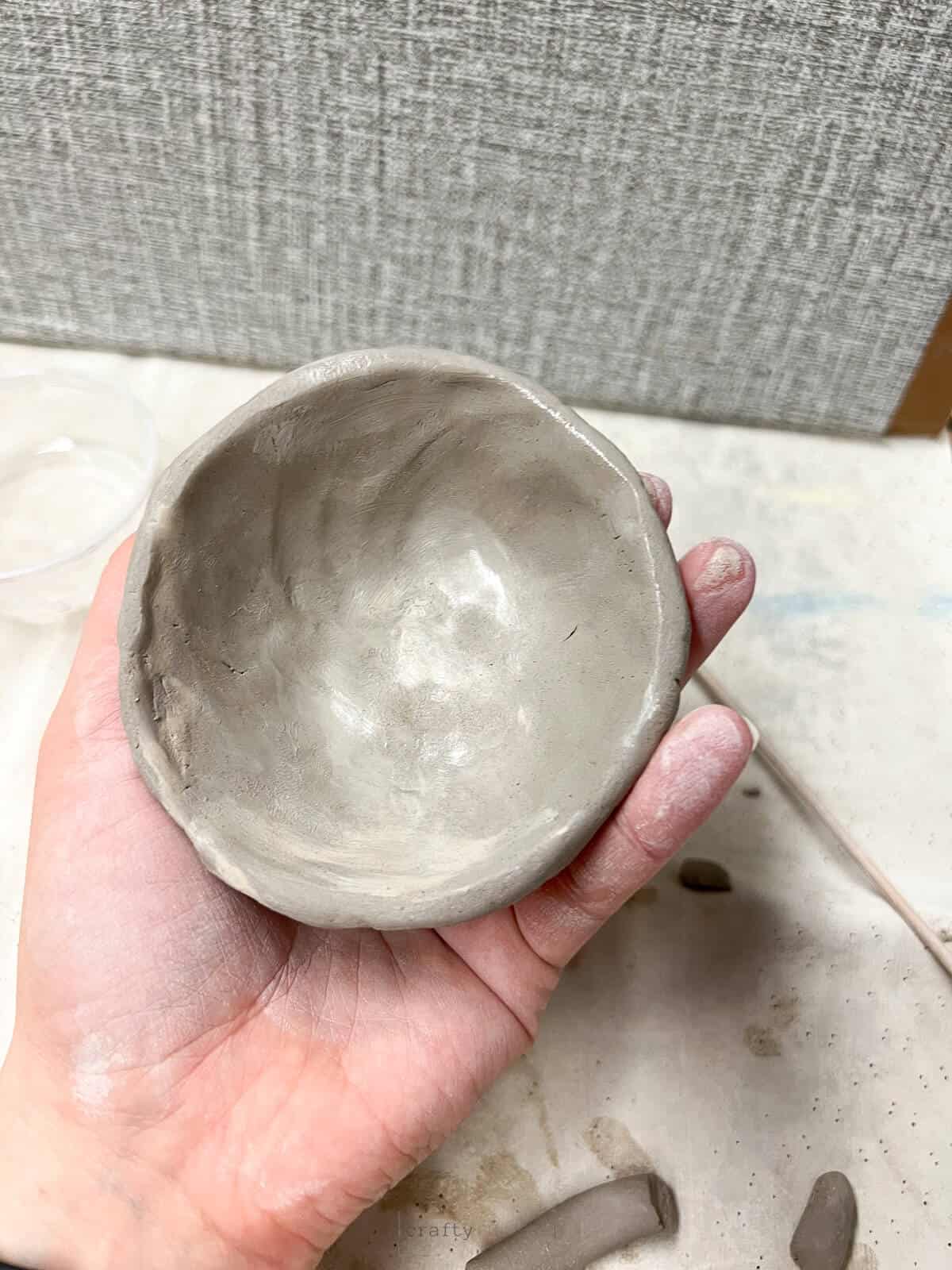 hand holding clay pinch pot smoothed out with water.