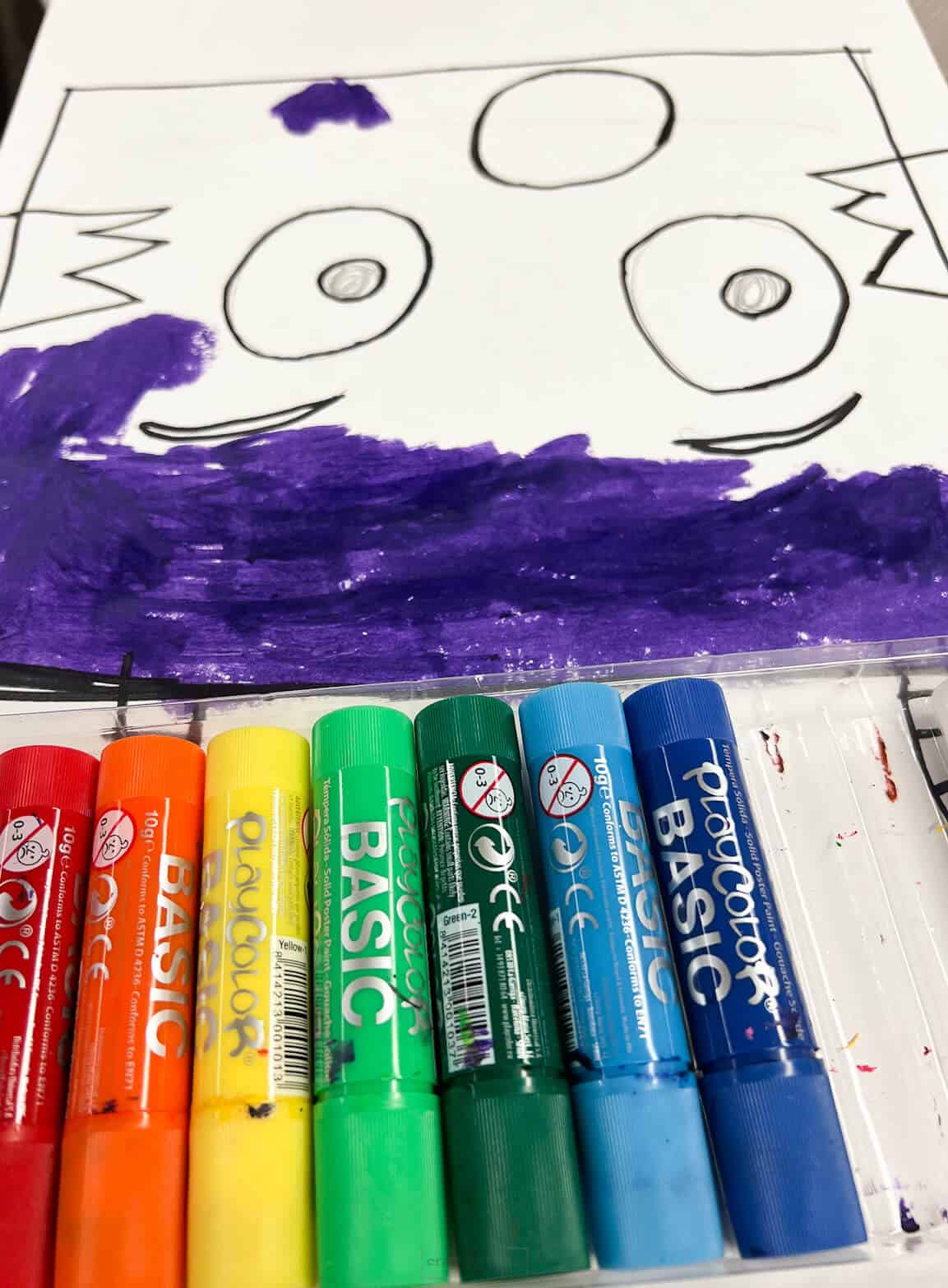 tempera paint sticks with monster drawing in the background.