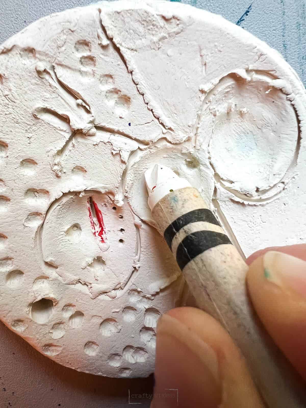 white crayon being applied to clay snowman slab.