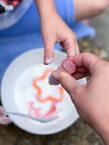 two hand adding red food coloring to homemade oobleck.