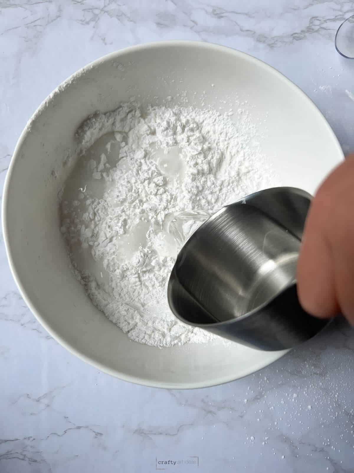 child'd hand pouring in 1/2 cup water to baby powder.