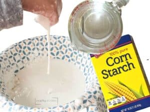 hand playing with oobleck slime and box of corn starch and measuring cup.