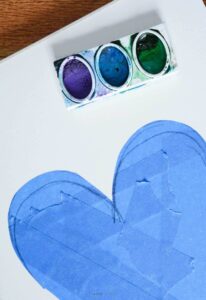 cool watercolor paint colors on white drawing paper with part of heart taped in blue painter's tape.