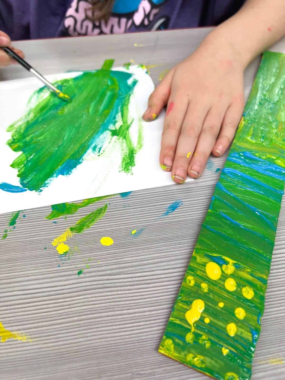 child's hand holding brush painting green and some patterns.