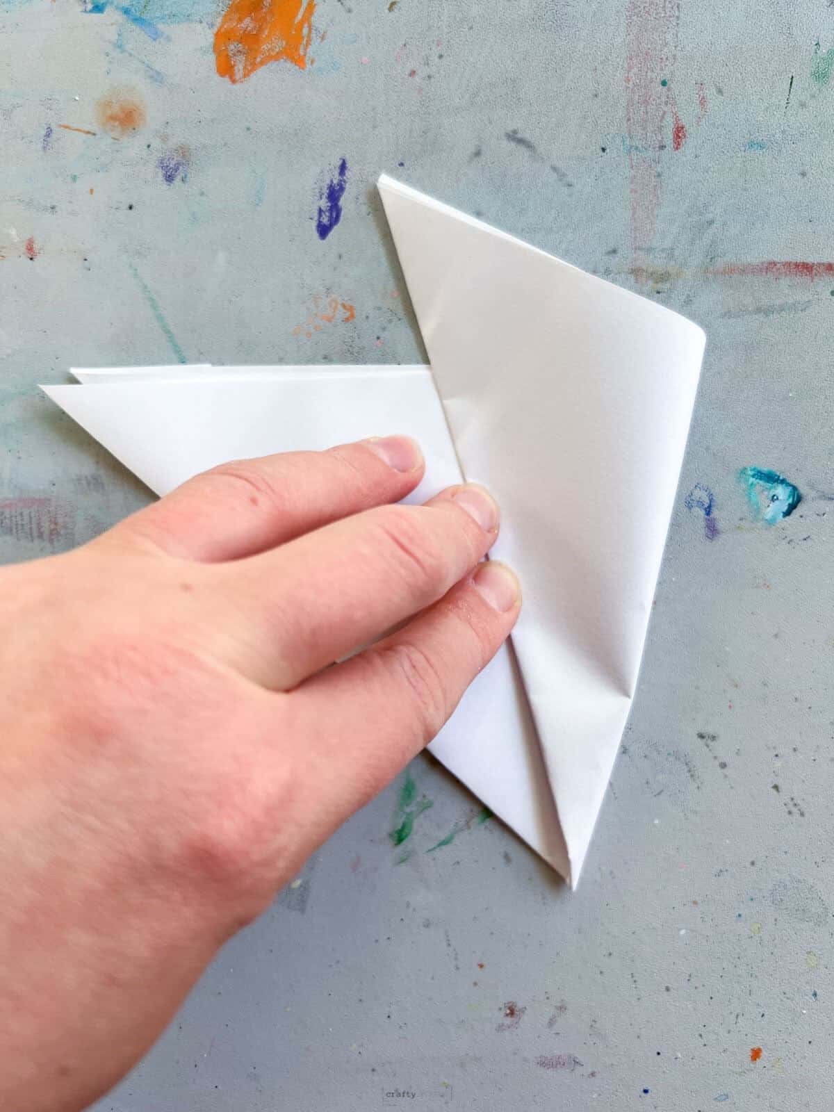 hand folding white paper triangle half way.