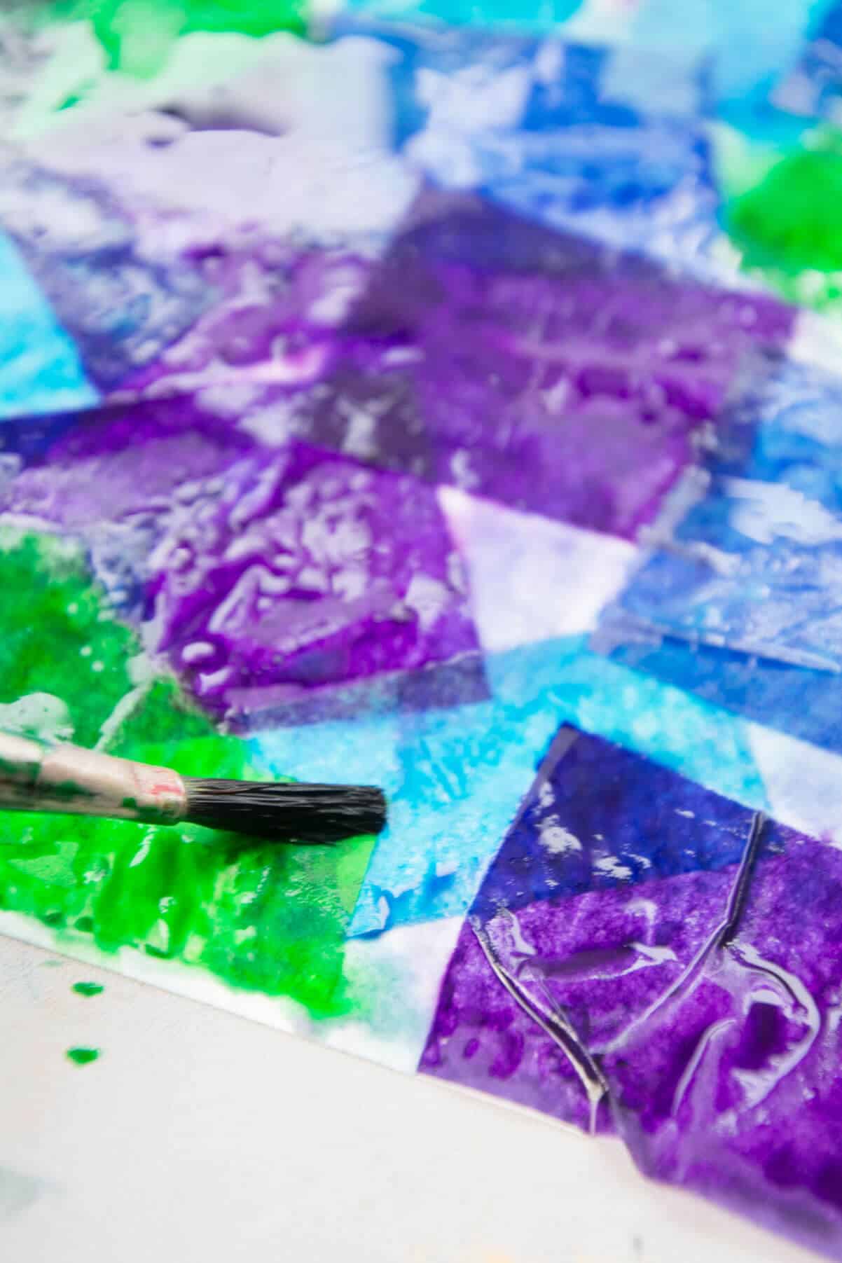 zoomed in view of bleeding tissue paper in green, purple and blue mixing together with brush painting water on.
