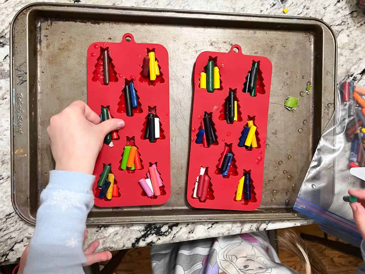 child's hand placing broken crayons in red silicone molds.