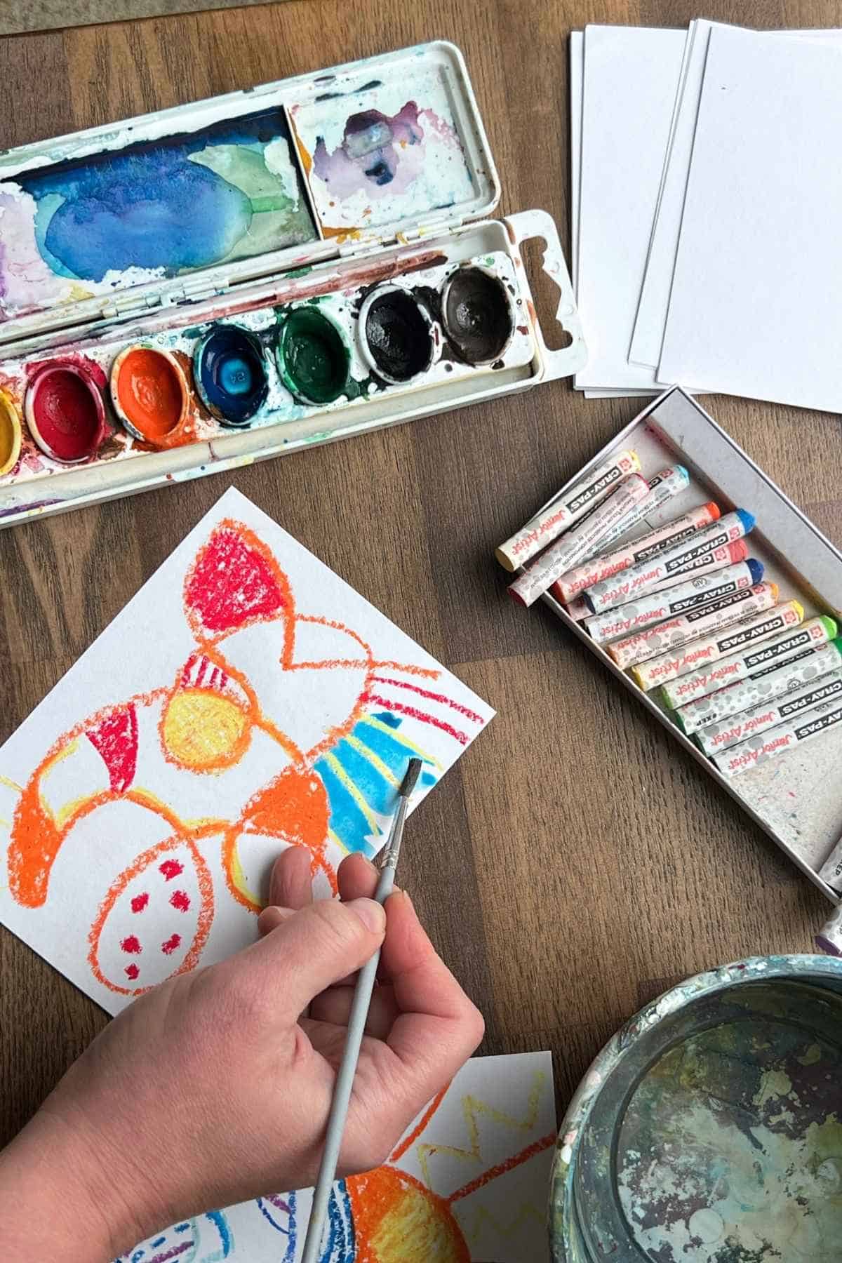 hand holding a brush to add watercolor paint to abstract art.