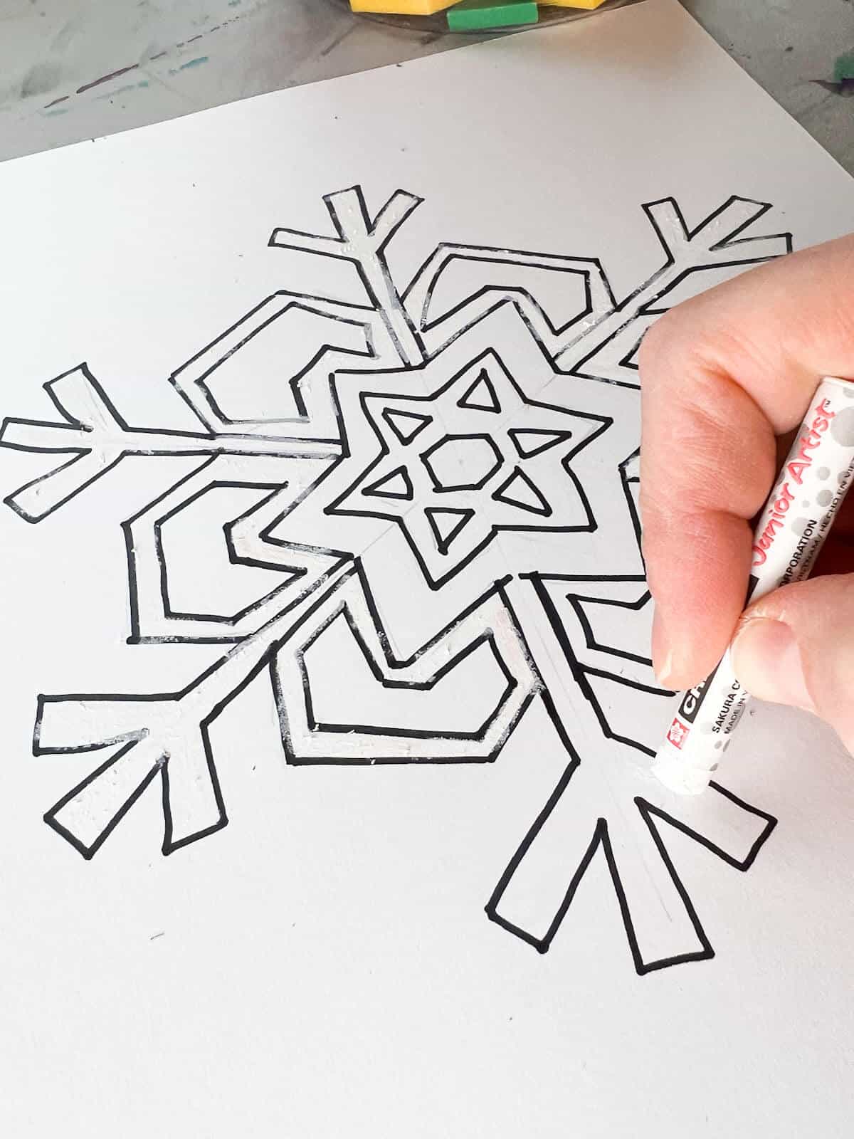 hand holding oil pastel coloring snowflake on white paper.