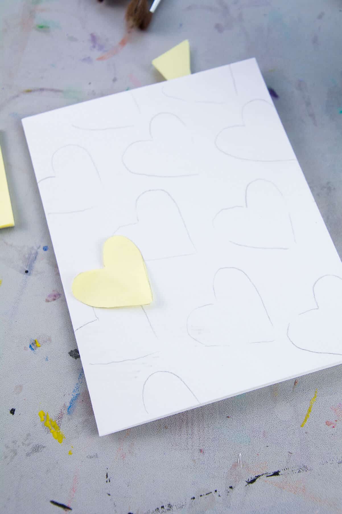 yellow paper heart sitting on white paper with hearts drawn in pencil.