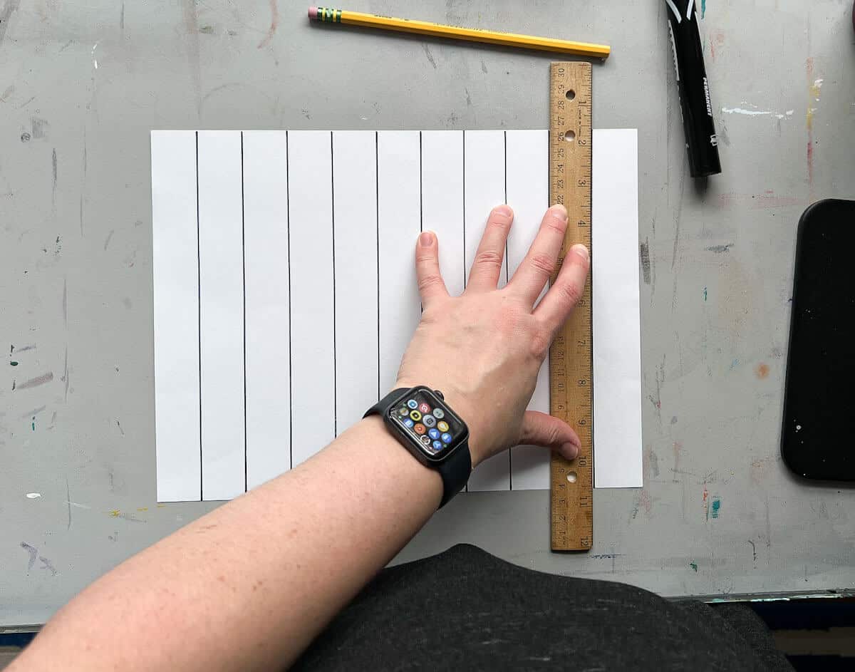 hand holding ruler on white paper with black lines.