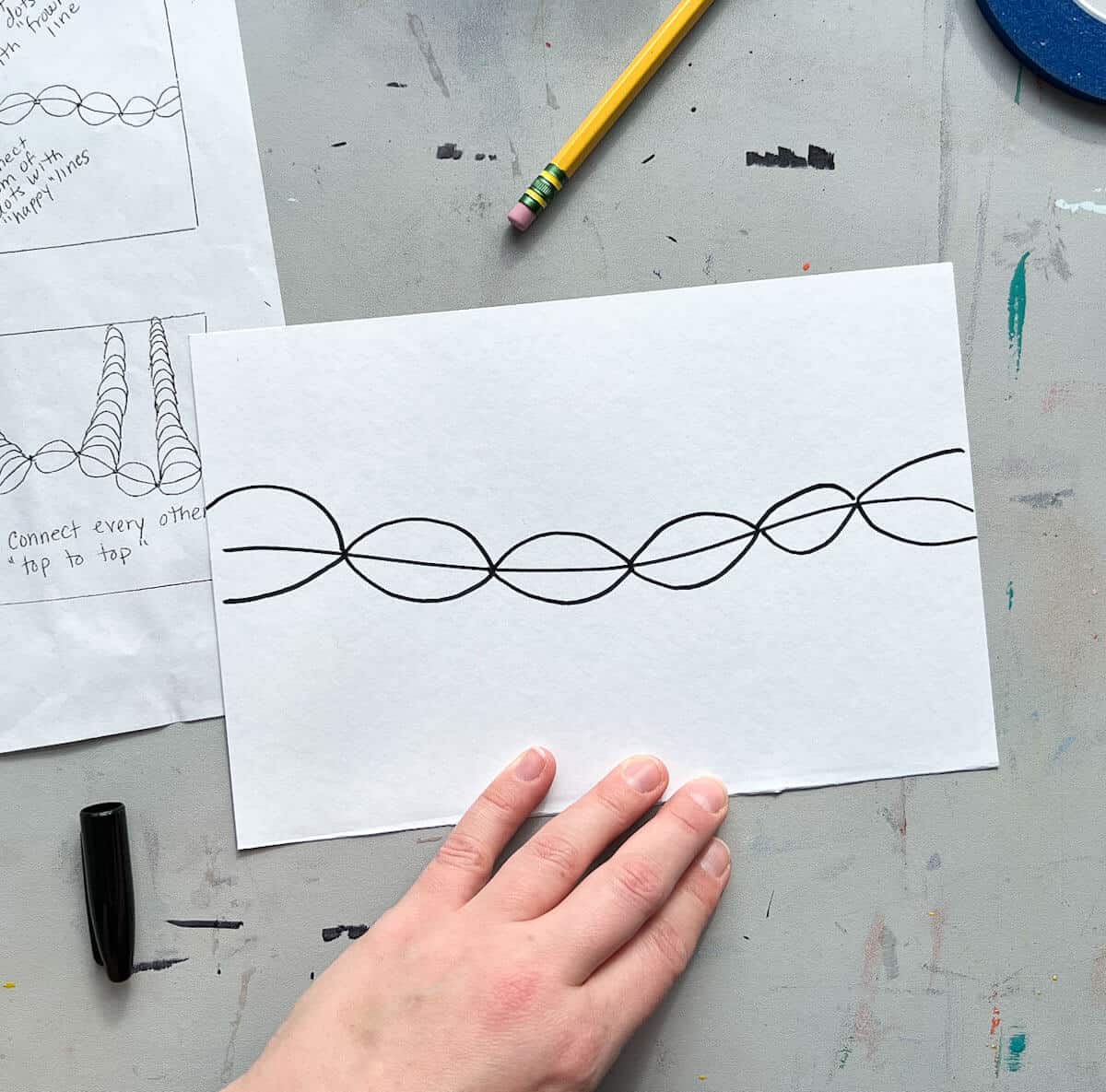 hand holding drawing paper with curved lines drawn across the middle in black marker.