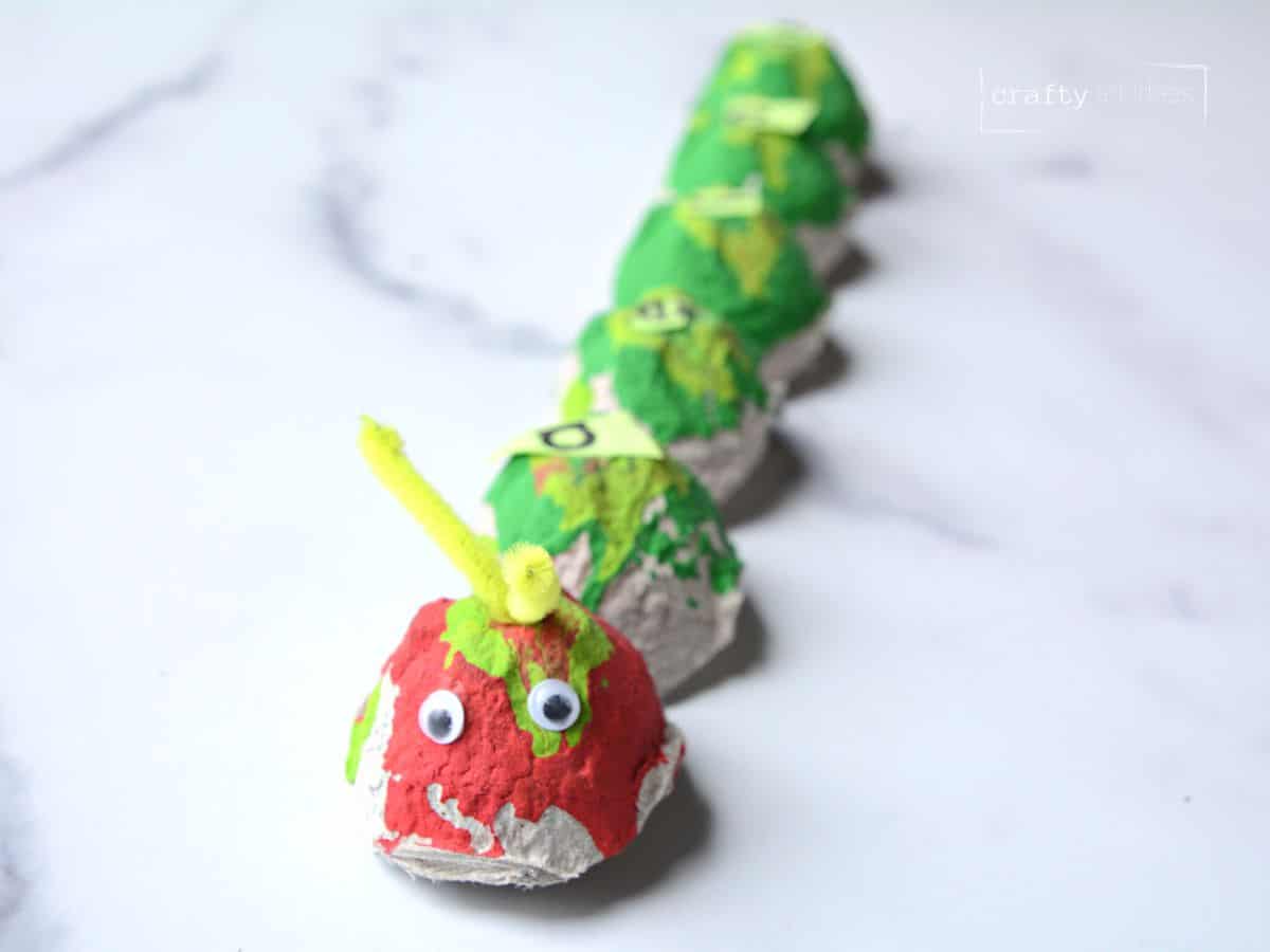 red and green painted egg carton caterpillar craft with googly eyes and pipe cleaner.