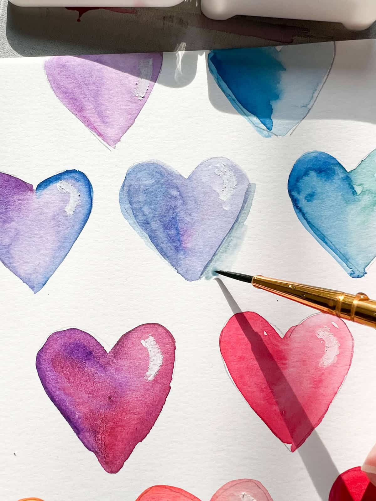 small brush adding gray blue paint to watercolor heart painting.
