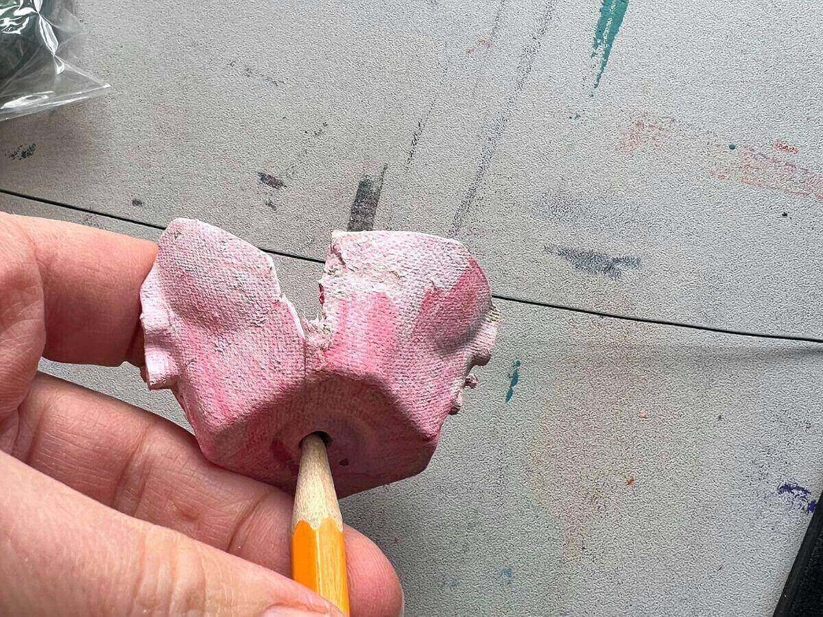 hand holding pencil poking hole into egg carton cut and painted to look like a flower.