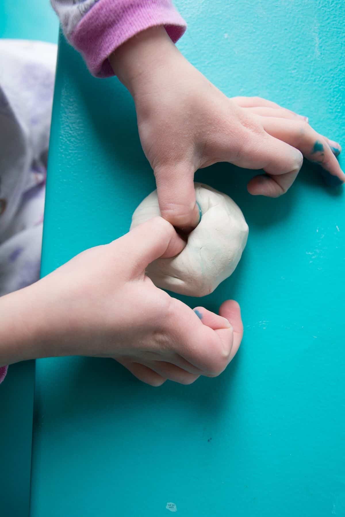 child's hand pushing thumbs into air dry clay ball.
