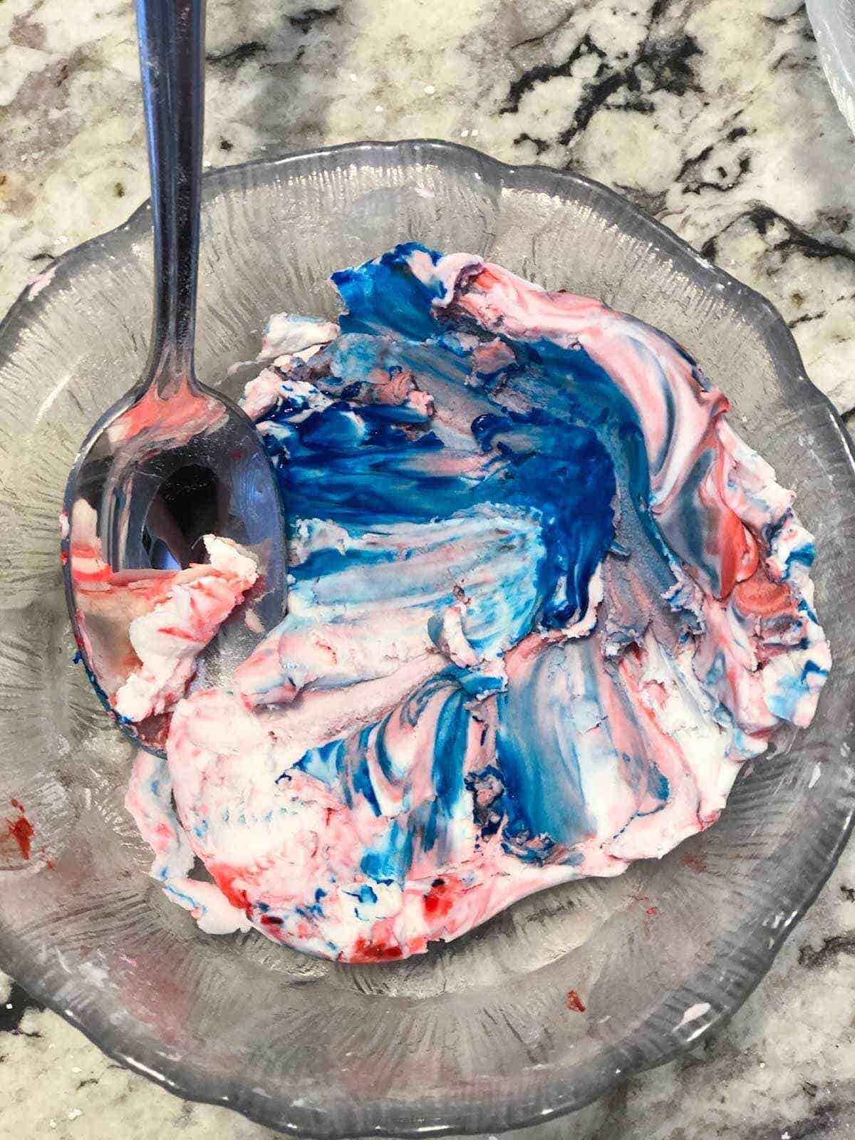 swirly red and blue dough in bowl with spoon.