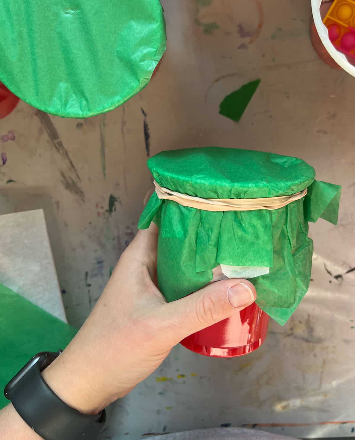 double-banded rubber band around cup with green tissue paper.