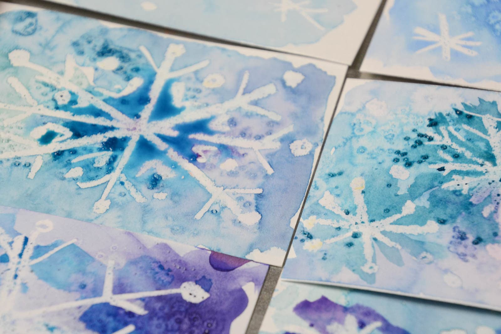 white snowflakes on small papers painted with blue and purple watercolor paint and salt.