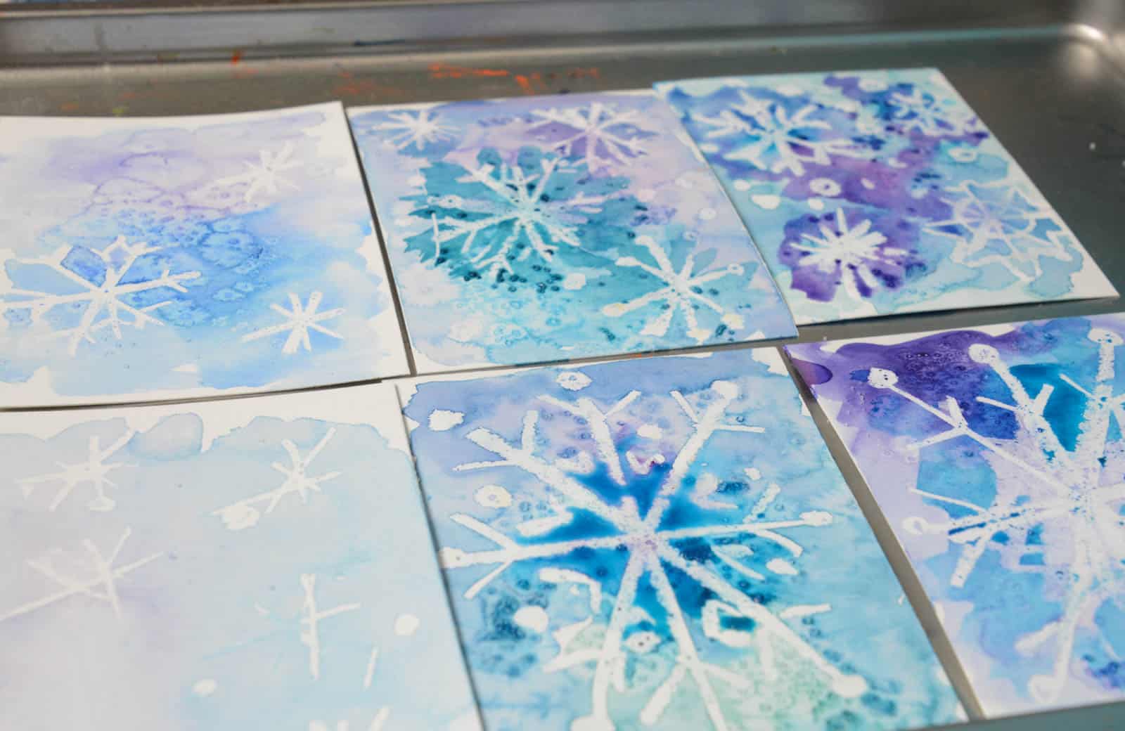 six small snowflake watercolor paintings with blue and purple skies.