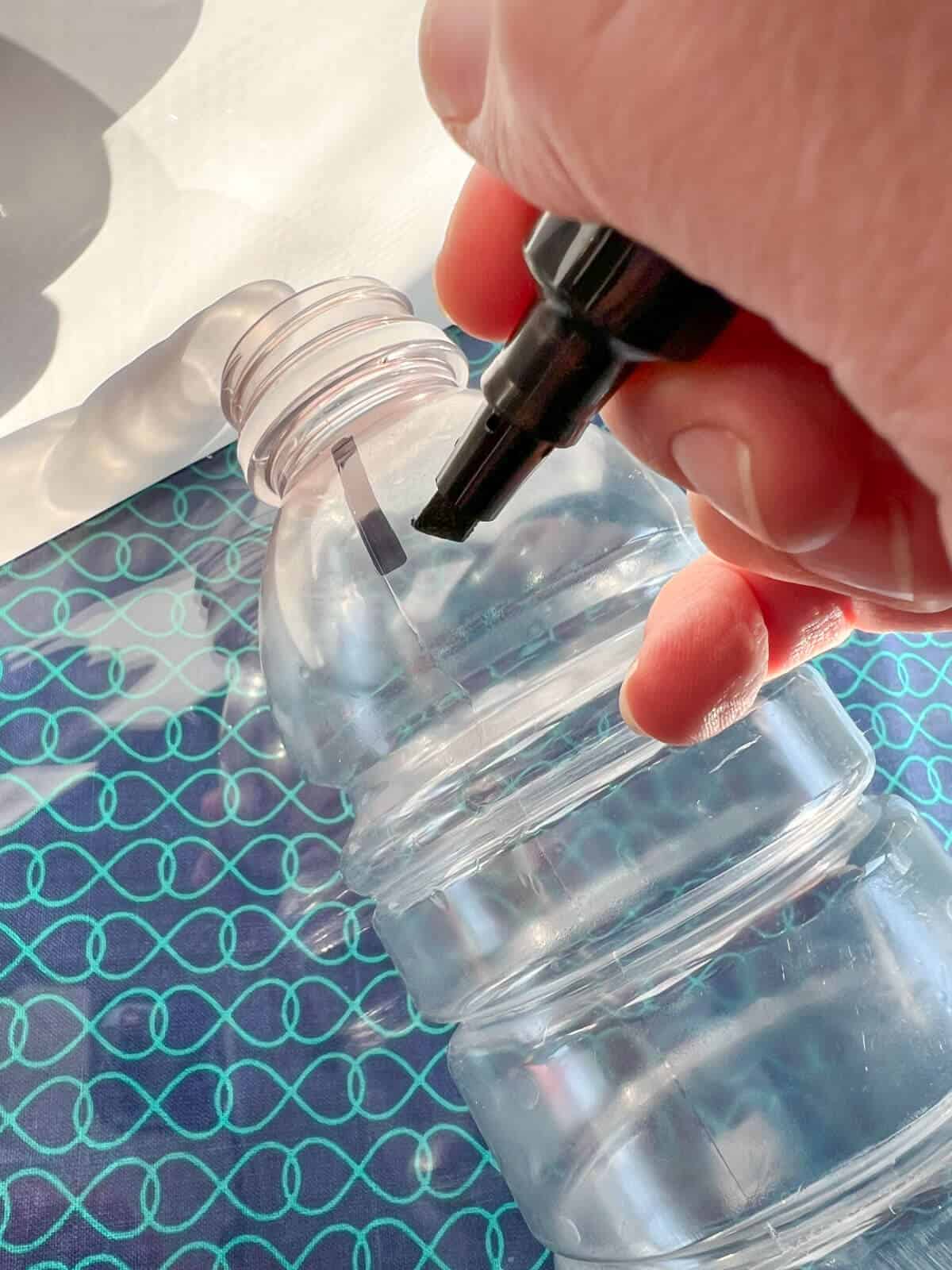 hand using black marker on plastic bottle.