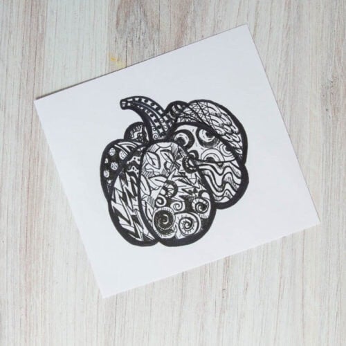 black and white pumpkin drawing with patterns and designs on wood table.