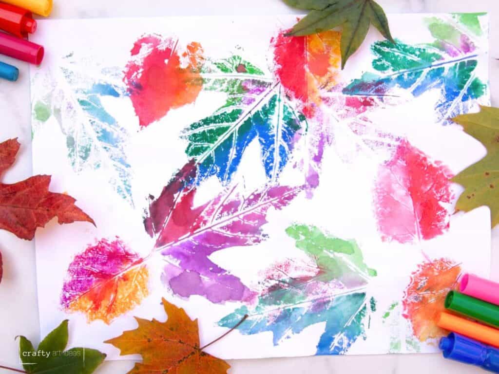 colorful leaf impressions on white paper with real leaves and markers on a table.