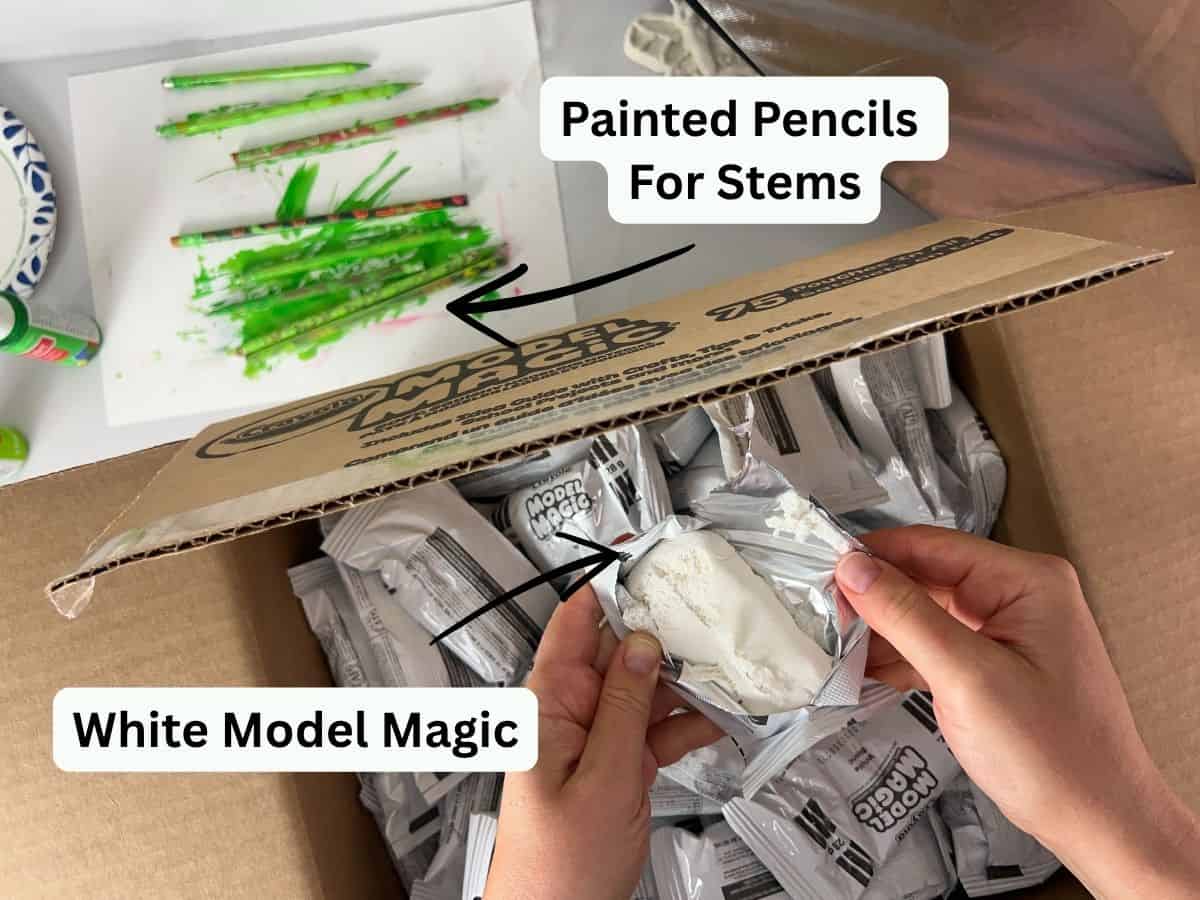 hands holding white Model Magic and paint green pencils in the background.