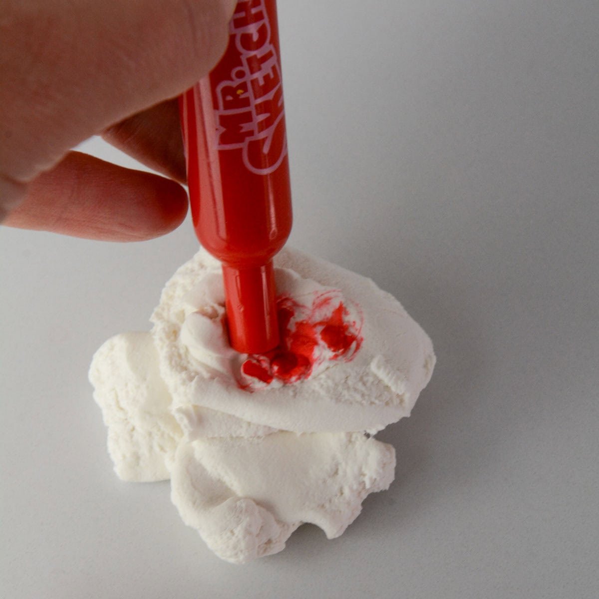 hand holding red marker adding it to a white dough.