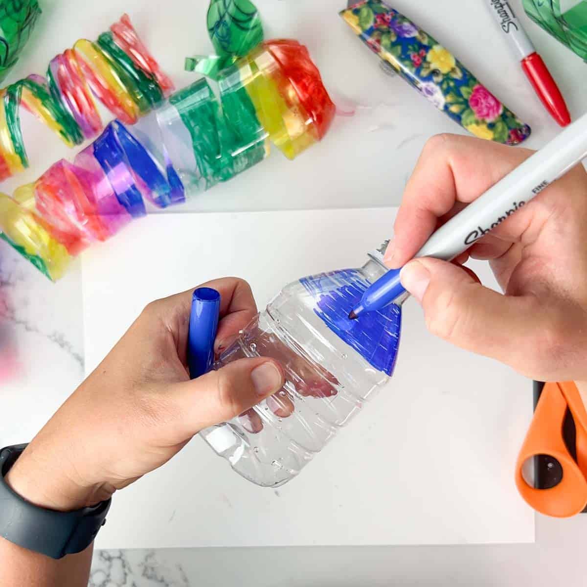 hands coloring a bottle with a blue marker.