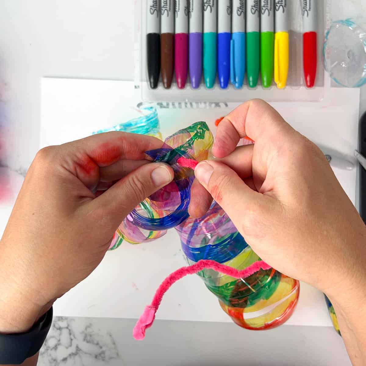 hand using hole punch to tie colored plastic bottle spirals together.