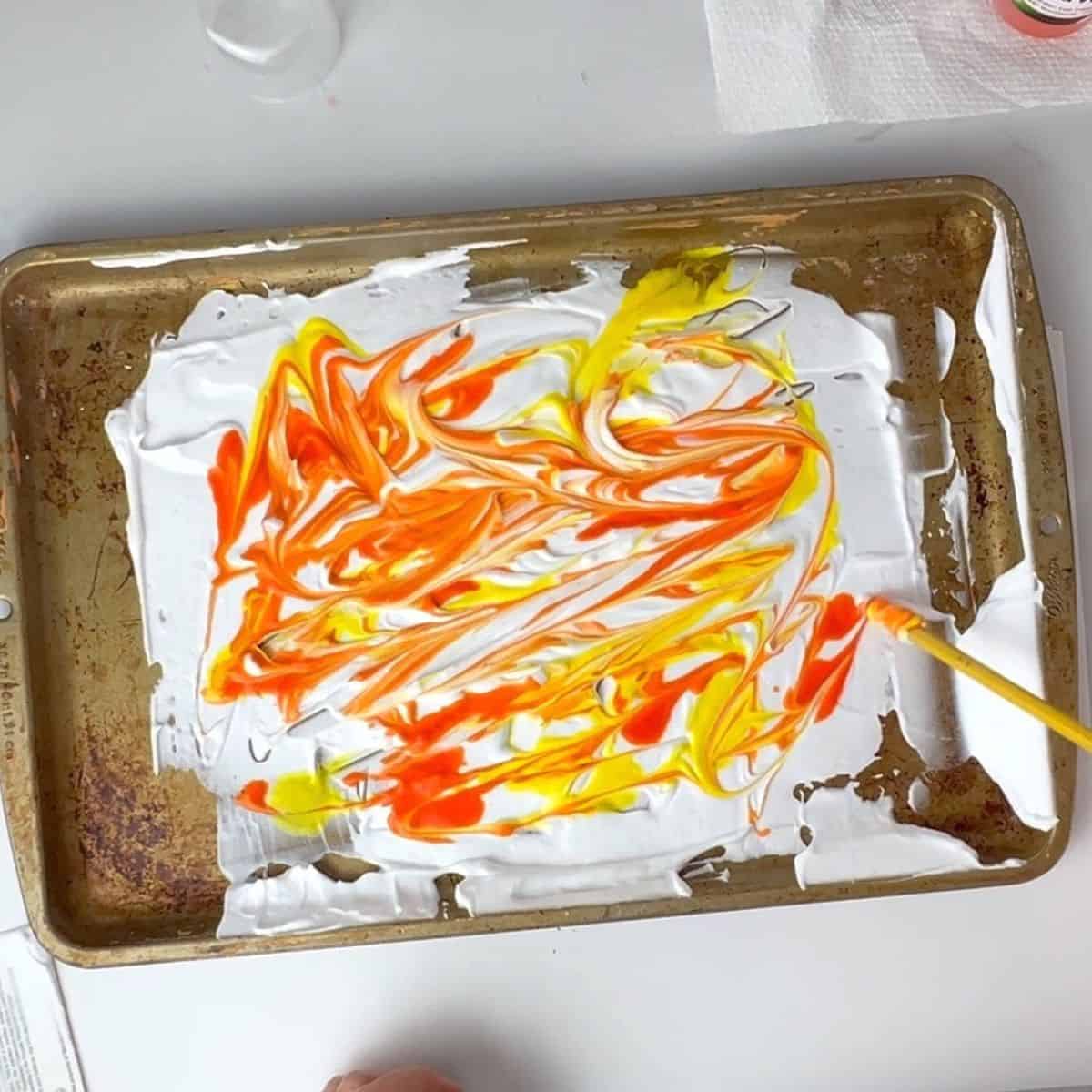 hand swirling orange and yellow watercolor paint on shaving cream.