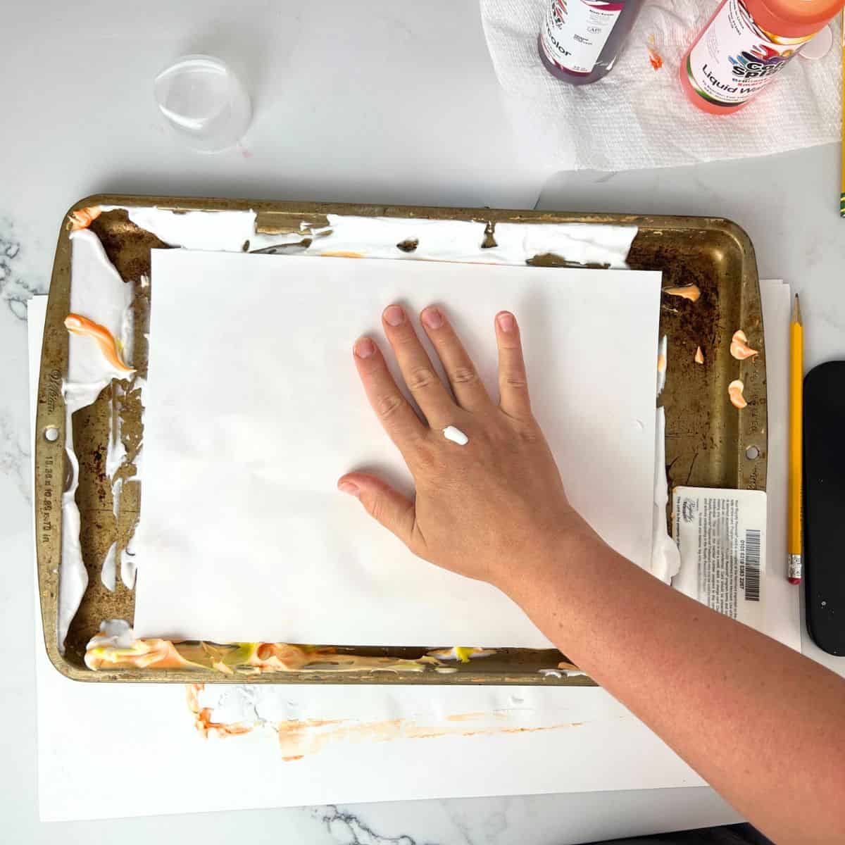hand pressing white paper into shaving cream paint.