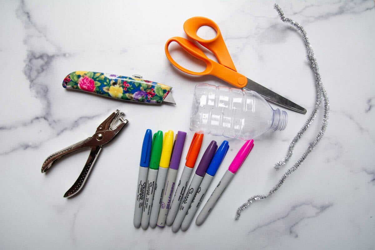 markers, hole puch, scissors and plastic bottle on a table.